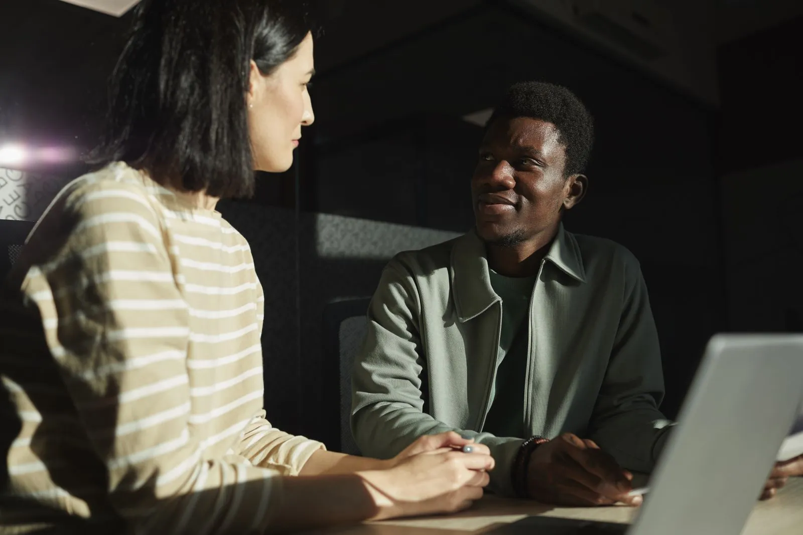 Two colleagues talking at a desk beside a laptop