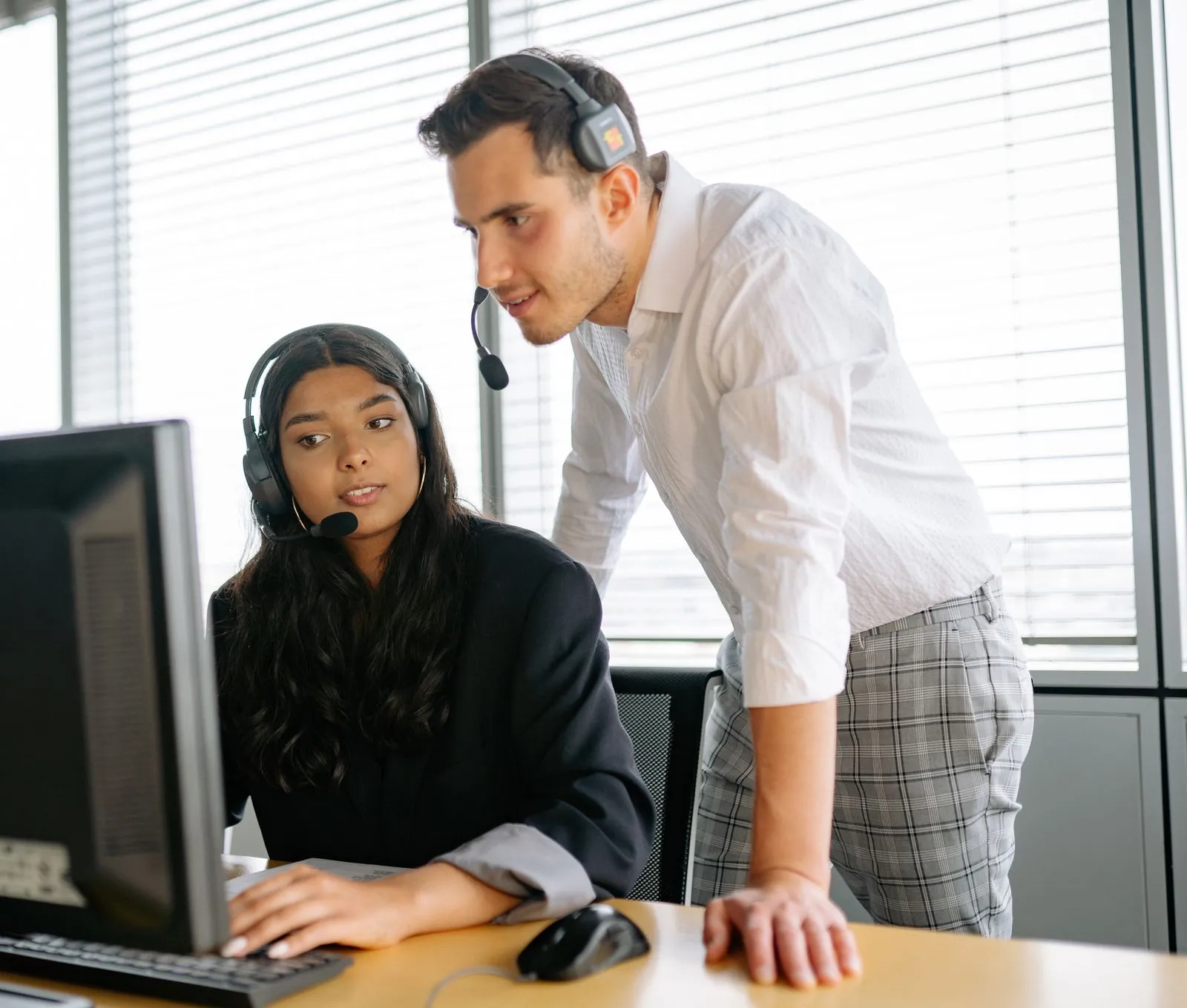 Two colleagues reviewing a computer workstation while wearing headsets